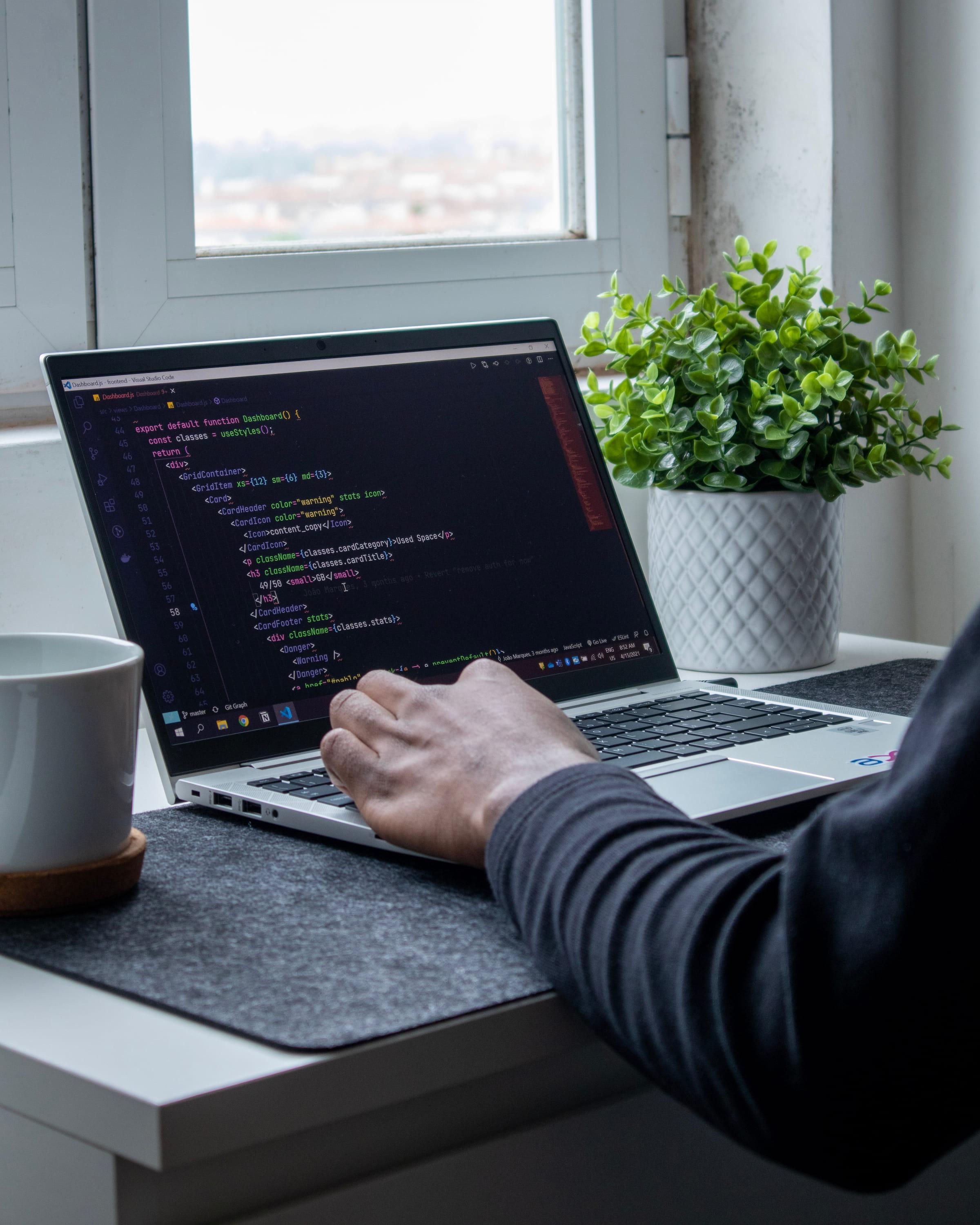 Ręka na klawiaturze laptopa z widocznym kodem na ekranie